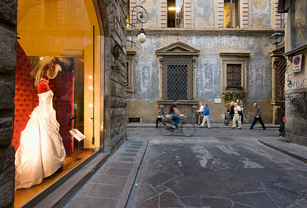 A dressmaker's window displays a gorgeous gown as shoppers stroll down an Italian street