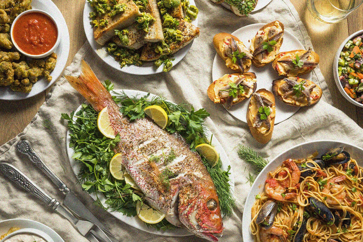 Top-down view of a table filled with plates of food, including fish, pasta with mussels, and bruschetta with anchovies